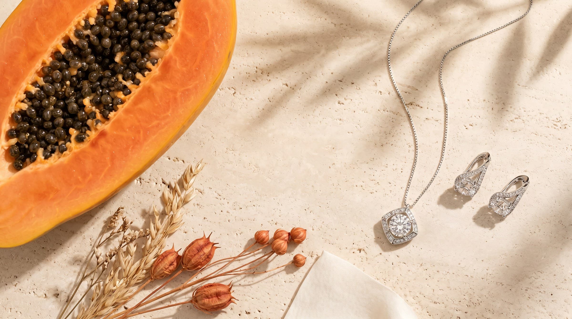 Joyas Alma y Sol sobre travertino con papaya y flores